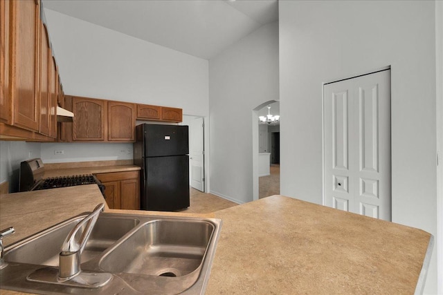 kitchen with sink, black refrigerator, high vaulted ceiling, range with gas cooktop, and a chandelier