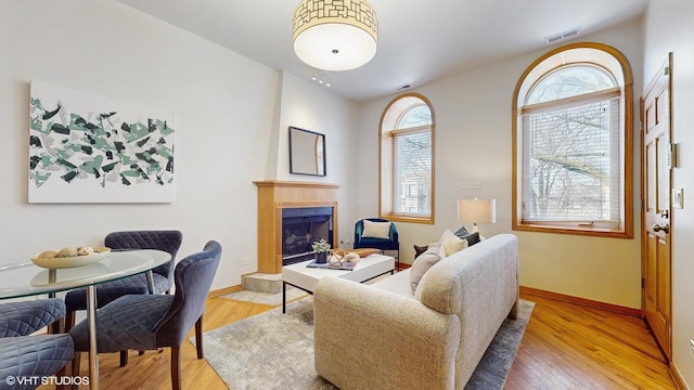 living room featuring visible vents, a fireplace, baseboards, and wood finished floors