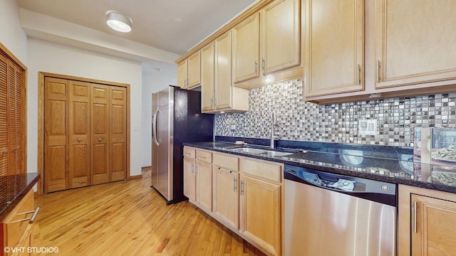 kitchen featuring stainless steel appliances, a sink, decorative backsplash, light wood finished floors, and dark stone countertops