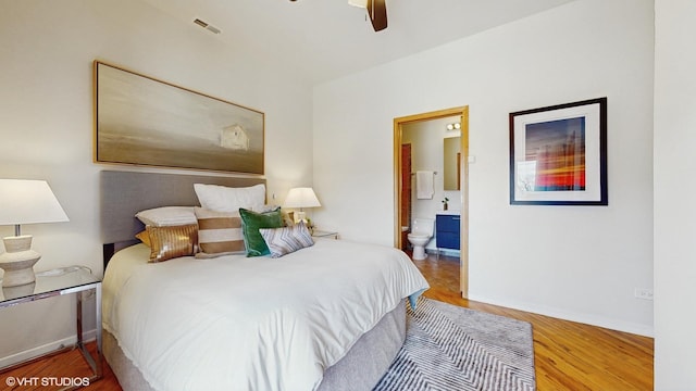 bedroom featuring ceiling fan, wood finished floors, visible vents, baseboards, and ensuite bath