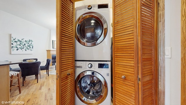 clothes washing area with light wood-type flooring, stacked washer and dryer, a fireplace, and laundry area