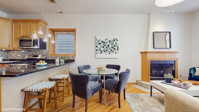 kitchen with visible vents, light wood-style flooring, appliances with stainless steel finishes, a kitchen breakfast bar, and backsplash