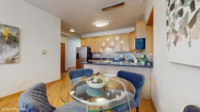 kitchen with tasteful backsplash, dark countertops, a peninsula, light wood-style floors, and stainless steel refrigerator with ice dispenser