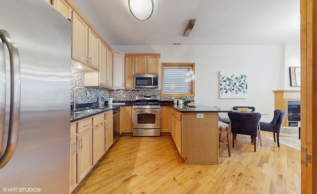 kitchen featuring stainless steel appliances, a sink, a peninsula, and light wood-style flooring