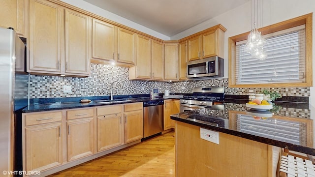 kitchen featuring dark stone countertops, appliances with stainless steel finishes, light wood-style flooring, and a sink