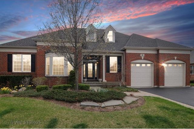 view of front of house with an attached garage, brick siding, a shingled roof, driveway, and a lawn