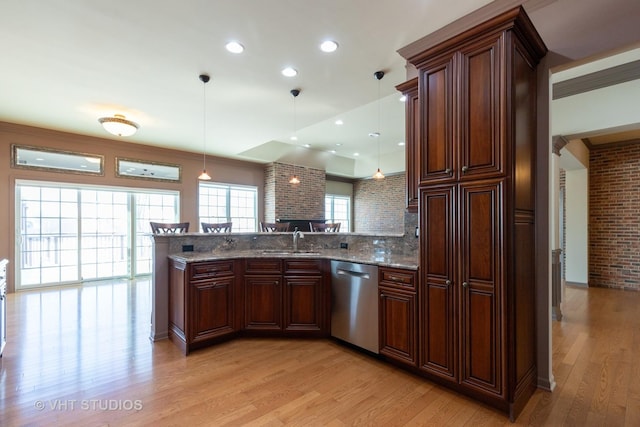 kitchen featuring pendant lighting, light wood finished floors, stainless steel dishwasher, a sink, and a peninsula