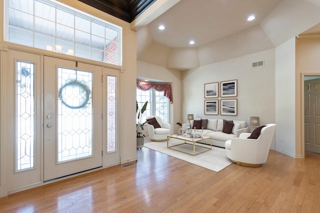 foyer entrance with a towering ceiling, light wood finished floors, and visible vents