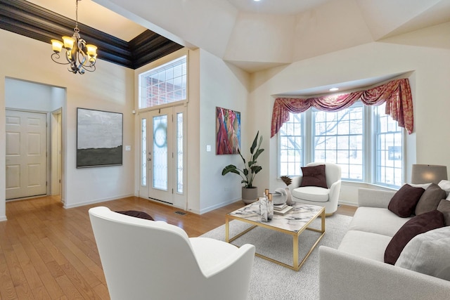 living area featuring a notable chandelier, a towering ceiling, baseboards, and wood finished floors