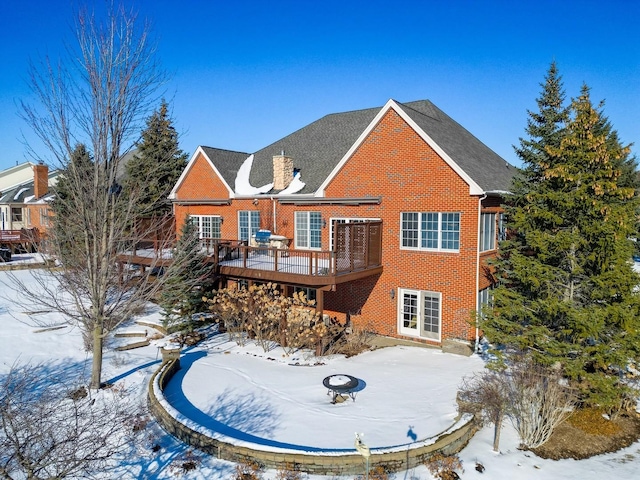 snow covered house with a patio, brick siding, and a wooden deck