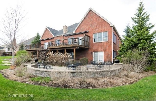 back of property with a chimney, a patio area, brick siding, and a deck