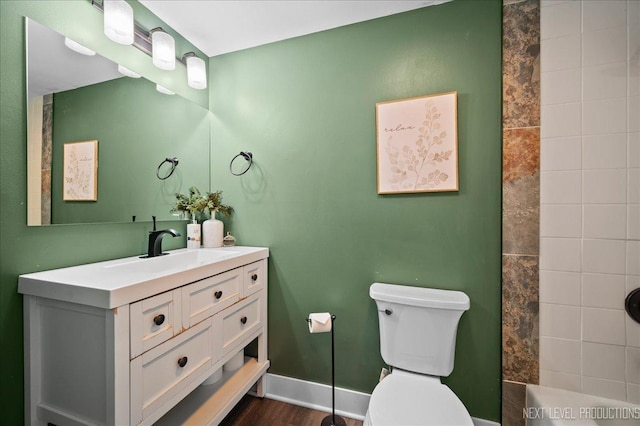 bathroom featuring hardwood / wood-style flooring, tiled shower, vanity, and toilet