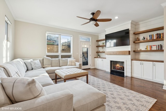 living room with dark wood-type flooring, ceiling fan, ornamental molding, and a fireplace