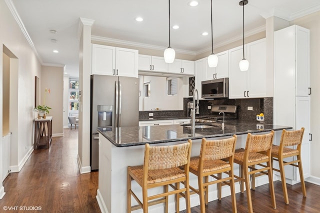 kitchen with dark wood-type flooring, a breakfast bar, appliances with stainless steel finishes, white cabinetry, and dark stone countertops