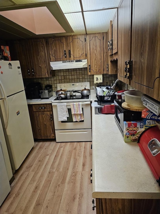 kitchen with tasteful backsplash, white appliances, sink, and light hardwood / wood-style flooring