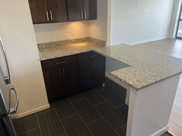 kitchen with light stone counters, dark brown cabinetry, and kitchen peninsula