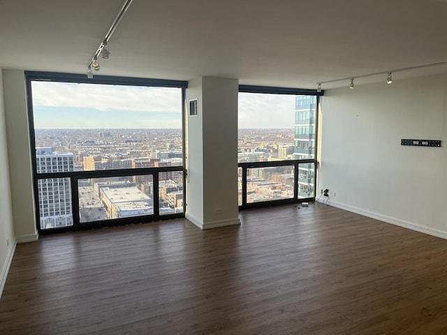 empty room with rail lighting, dark hardwood / wood-style floors, and a wall of windows