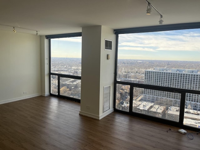 empty room featuring expansive windows, rail lighting, and dark hardwood / wood-style flooring