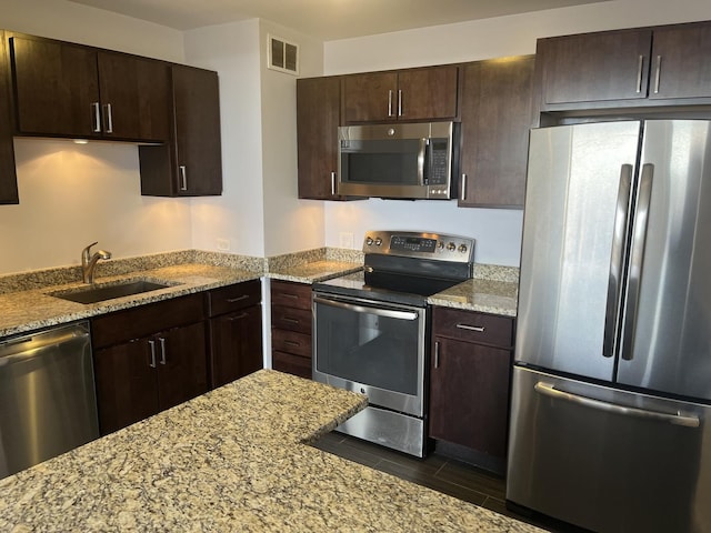 kitchen with dark brown cabinetry, sink, light stone countertops, and appliances with stainless steel finishes