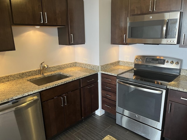 kitchen with light stone counters, sink, dark brown cabinetry, and appliances with stainless steel finishes