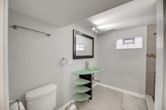 bathroom with visible vents, toilet, a sink, baseboards, and walk in shower