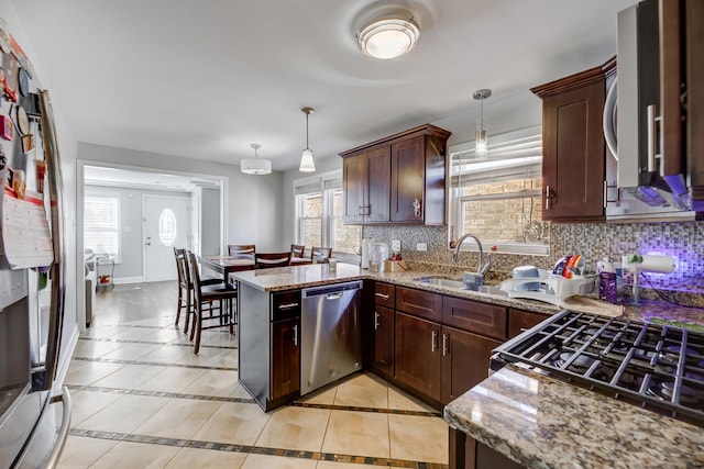 kitchen featuring light stone counters, stainless steel appliances, tasteful backsplash, a sink, and a peninsula