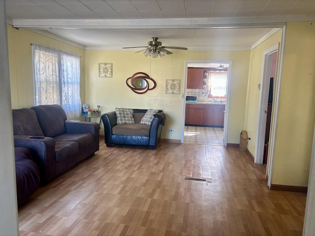 living room featuring ceiling fan, ornamental molding, and light wood-type flooring