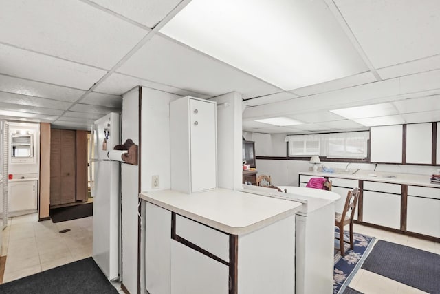 kitchen featuring a drop ceiling, kitchen peninsula, white cabinets, and light tile patterned flooring