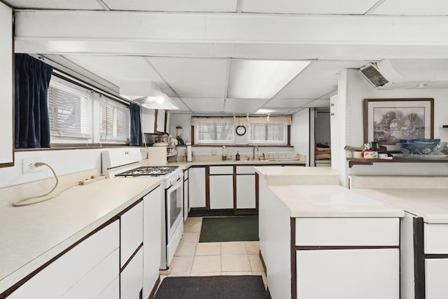 kitchen with sink, white gas stove, white cabinets, and light tile patterned floors