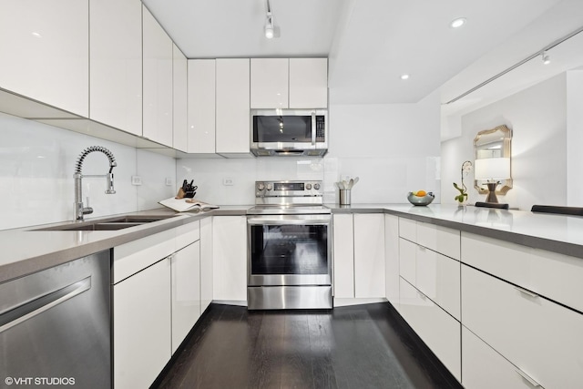 kitchen with stainless steel appliances, dark wood-type flooring, a sink, white cabinets, and modern cabinets