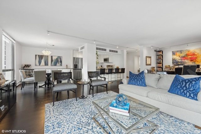 living room with an inviting chandelier, dark wood finished floors, visible vents, and track lighting