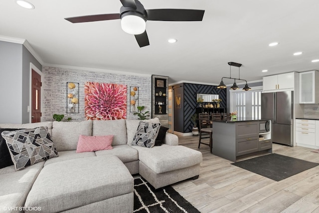 living area featuring light wood finished floors, recessed lighting, ornamental molding, ceiling fan, and brick wall