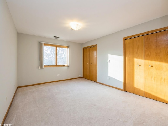 unfurnished bedroom featuring baseboards, two closets, visible vents, and light colored carpet