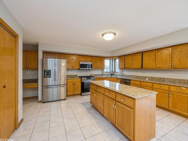 kitchen featuring brown cabinetry, a kitchen island, appliances with stainless steel finishes, light stone countertops, and a sink