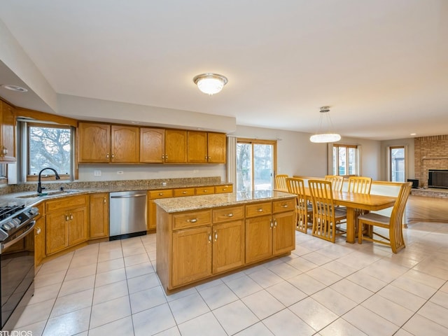 kitchen featuring light stone counters, brown cabinets, stainless steel dishwasher, a sink, and gas range