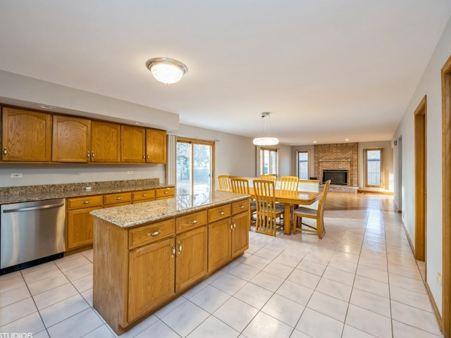 kitchen with light tile patterned floors, light stone counters, a fireplace, dishwasher, and brown cabinetry