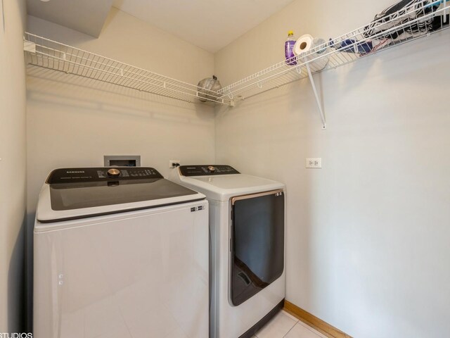 clothes washing area featuring laundry area, light tile patterned flooring, washer and clothes dryer, and baseboards
