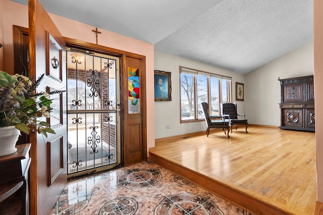 entrance foyer featuring vaulted ceiling, wood-type flooring, and a textured ceiling