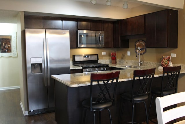 kitchen featuring sink, appliances with stainless steel finishes, dark brown cabinets, light stone counters, and a kitchen bar