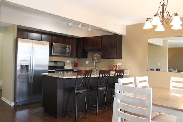 kitchen with dark wood-type flooring, a kitchen bar, decorative light fixtures, dark brown cabinets, and appliances with stainless steel finishes