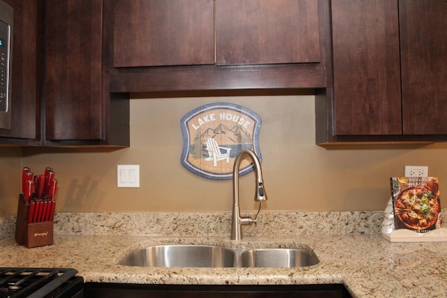 kitchen featuring dark brown cabinetry, light stone countertops, and sink