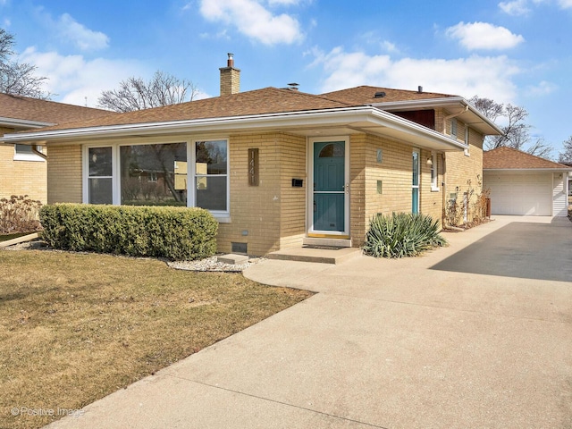 view of front of house featuring brick siding, a chimney, a front lawn, and an outdoor structure