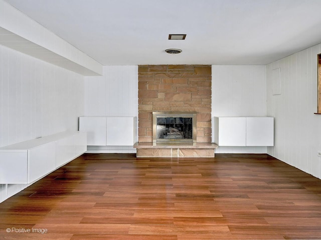 unfurnished living room with a stone fireplace, visible vents, and wood finished floors