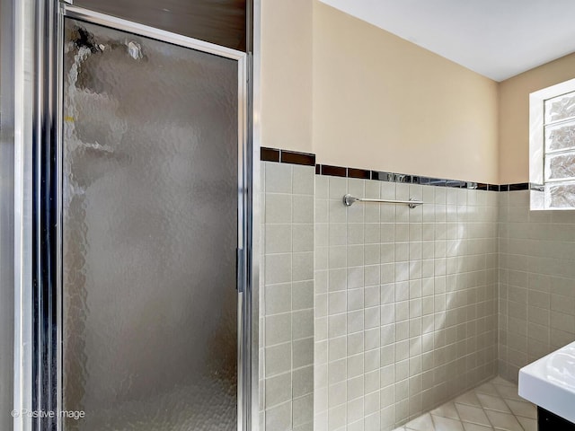 bathroom featuring tile patterned floors, a wainscoted wall, tile walls, and a stall shower