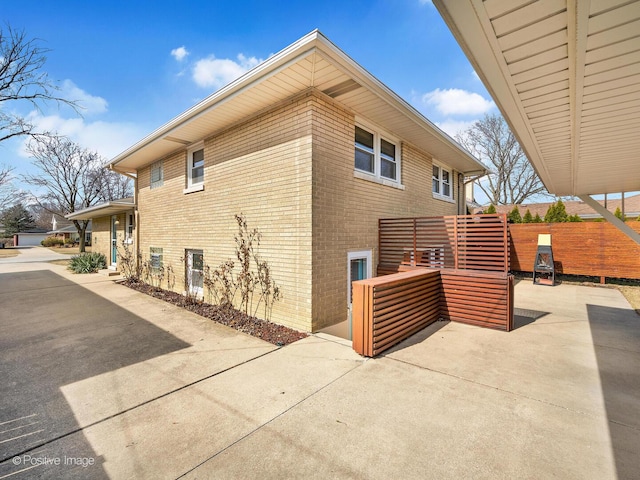 view of side of home with fence, brick siding, and a patio area