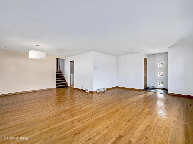 unfurnished room with stairway, baseboards, light wood-style floors, and visible vents