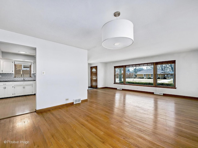 unfurnished living room featuring visible vents, baseboards, light wood-style floors, and a sink