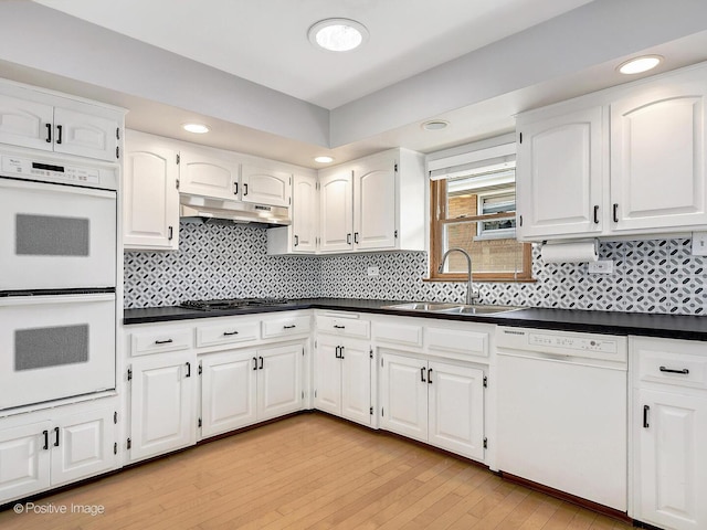 kitchen with white appliances, a sink, under cabinet range hood, white cabinetry, and dark countertops