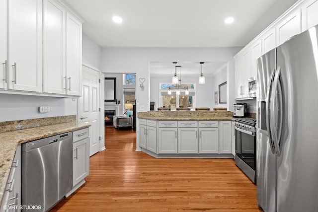 kitchen with white cabinetry, pendant lighting, stainless steel appliances, and light hardwood / wood-style floors