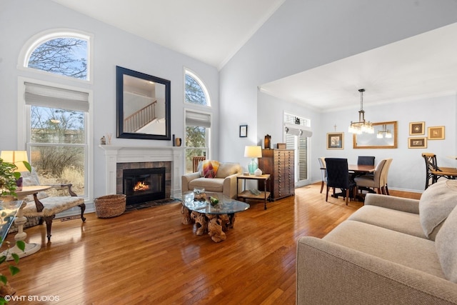 living room with an inviting chandelier, crown molding, high vaulted ceiling, a tile fireplace, and hardwood / wood-style floors